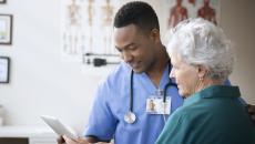 Doctor and patient look at a tablet while conversing.