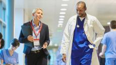 Doctor and healthcare worker talking in hospital hallway.