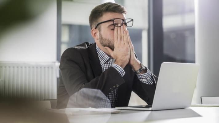 worker rubbing eyes at laptop