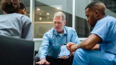 Doctor with tablet talking to seated coworkers