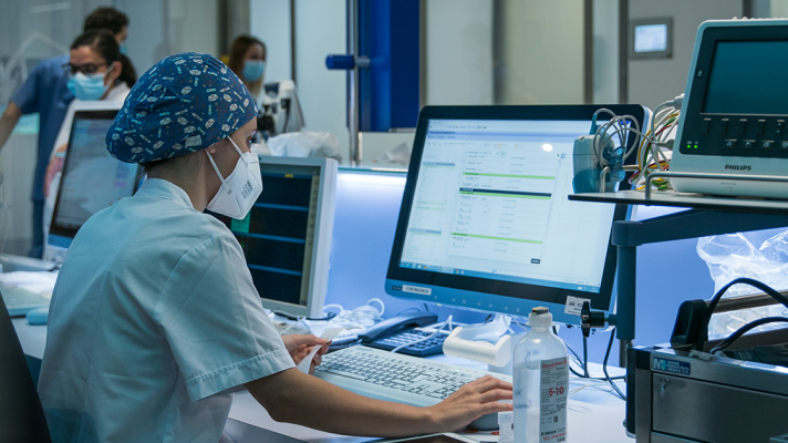 Person in medical wear in PPE at computer in hospital